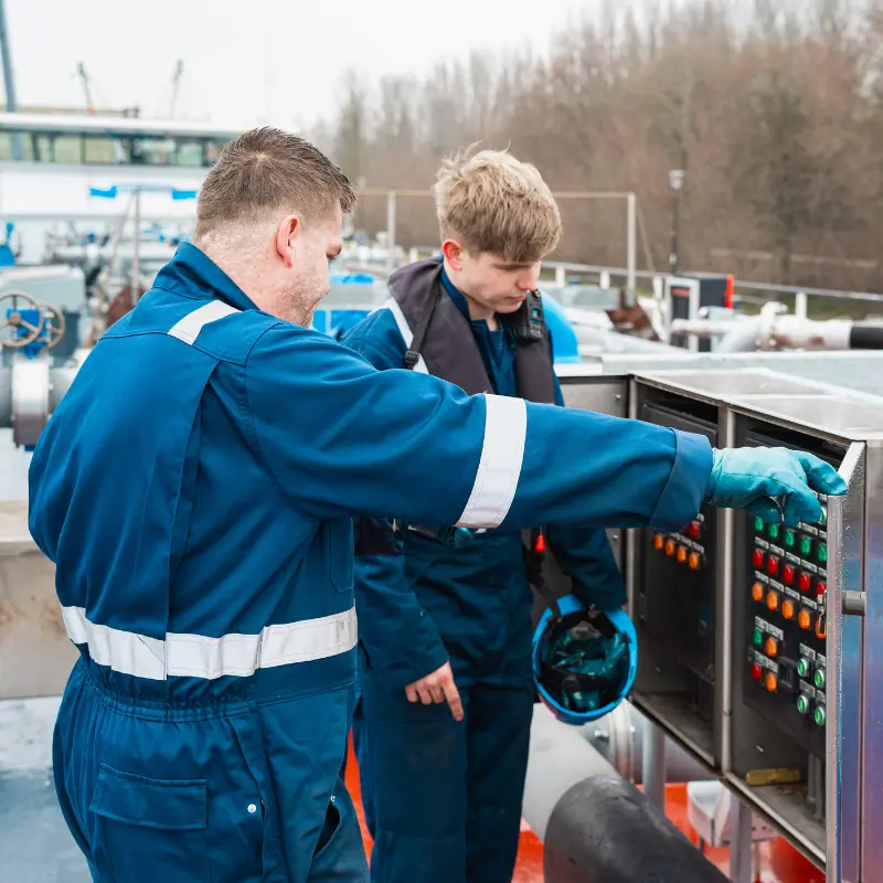 Ervaren medewerker van A. de Groot geeft een jonge collega uitleg over de bediening aan boord