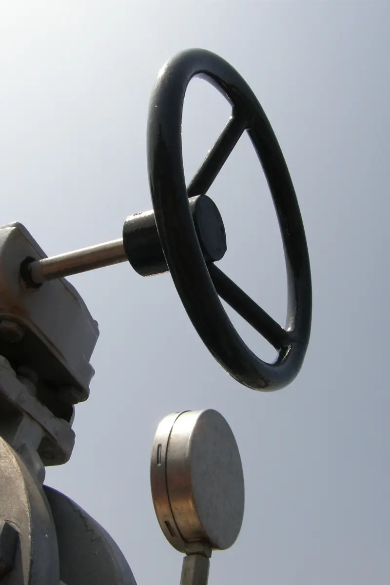 Close-up van een zwart bedieningswiel en drukmeter op een installatie aan boord van een binnenvaartschip.