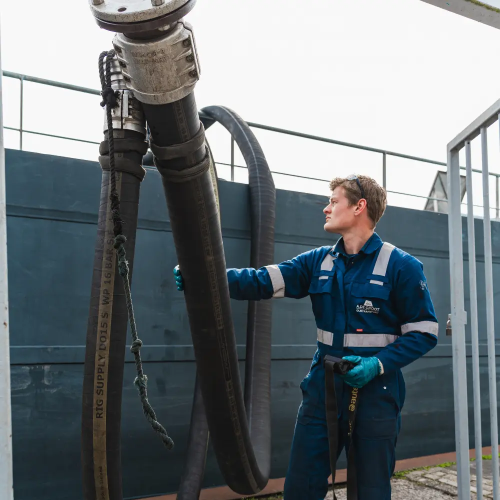 Medewerker van A. de Groot werkt met laad- en losslangen aan boord van een binnenvaartschip.