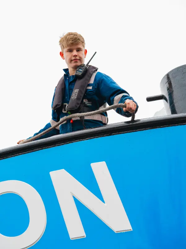 Medewerker van A. de Groot werkt met een touw op het dek van een binnenvaartschip.